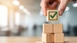 © DesignGallery - Hand placing final wooden block with green checkmark on stacked cubes