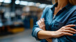 © Laura - Confident female worker standing with arms crossed in a warehouse, faceless, industrial shelves blurred, with copy space