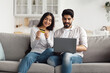 © Prostock-studio - Favorite online store, delivery goods at home and shopping together. Domestic shopaholic concept. Happy young arab male and lady with laptop and credit card pay order, on sofa in living room interior