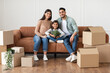 © Prostock-studio - House Move And Renovation Concept. Portrait of happy loving family of three people sitting on the couch in new empty apartment, posing and looking at camera, parents embracing girl holding plant