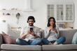 © Prostock-studio - Audio app, online music, play online game and enjoy free time at home. Smiling millennial arab lady and bearded guy in wireless headphones typing message on smartphones in living room interior