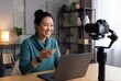 © Meow Creations - Cheerful asian woman filming video blog content with camera and laptop in modern home office