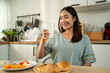 © Kawee - Asian attractive woman drinking a glass of white milk in kitchen at home.