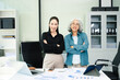 © Nuttapong punna - Confident Asian businesswomen standing in modern office. Leadership, teamwork, mentoring and corporate success concept with laptop and documents.