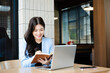 © Nuttapong punna - Asian businesswoman working online with laptop and notebook. Remote work, productivity, learning and freelance lifestyle concept in modern workspace