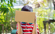 © Kunlathida - Shot of a young Asian boy standing outdoor and holding up a cardboard box to cover his face