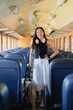 © Tj - Asian woman smiling as she walks the train aisle pulling a suitcase, ready for a commute or journey; modern, confident traveler enjoying convenient, stylish public transport