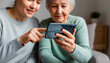 © Iuliia - Elderly woman and adult daughter holding and looking at a smartphone. Senior couple using tech device with help of woman. Digital connection and modern communication for older generation.