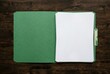 © Evgenia - Green folder with blank white sheets of paper inside, resting on a dark wooden surface, providing a clean and organized workspace for documents and notes