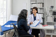 © Wasan - Female doctor explaining medical checkup results to patient in hospital room, showing medical checkup results to senior patient in hospital room, discussing diagnosis and treatment plan.
