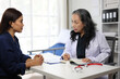 © Wasan - Senior female doctor taking notes while listening to patient in hospital room.