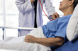 © Wasan - Female doctor examining a senior patient lying in hospital bed using a stethoscope.