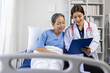 © Wasan - Asian doctor showing medical results to elderly patient in hospital bed.