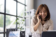 © Wasan - Asian businesswoman talking on phone and working on laptop in office.