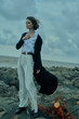 © SHOTPRIME STUDIO - Fashionable woman on a rocky coast, wind in her coat, white shirt and wide trousers, dramatic sea backdrop emphasizing style and resilience