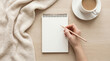 © MOHAMED - Writing check list concept. Pov top above overhead close up view photo of female hand making notes in empty notepad near white plaid and hot cup of coffee