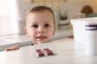 © New Africa - Child safety at home. Little boy playing with pills at table in kitchen, closeup