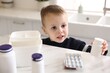 © New Africa - Child safety at home. Little boy playing with pills at table in kitchen