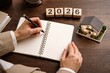 © Olga Ко - Woman hands writing in notebook with 2026 blocks and small house model, concept of real estate investment, mortgage planning and home insurance.