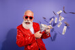 © deagreez - Energetic retired showman in red jacket counts money while tossing bills at a purple studio backdrop during a festive party vibe