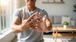 © Mila Shnobel - Man experiencing arthritis pain in hands, stretching fingers in bright living room, showcasing discomfort and the need for relief in a cozy home environment