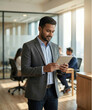 © suryansh - Confident Indian male manager working on a tablet or laptop inside a modern glass-walled corporate office. He is dressed in professional Western or Indo-Western business attire