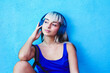 © VISTA by Westend61 - Woman in blue tank top with headphones listening to music by blue wall