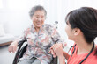 © kapinon - 病院や訪問介護で車椅子の高齢者を看護師が支える手を握る見つめ合うイメージ