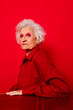 © VISTA by Westend61 - Stylish woman in red shirt with white hair and bold makeup against a red background