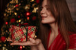 © svetograph - Woman holding christmas gift standing near glowing festive tree