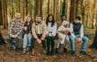 © Reuben - A group of people are sitting on a bench in a forest. They are all smiling and holding cups