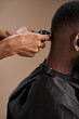 © The Yudel Media - Close-up view of a professional barber using electric clippers to trim the back of an adult Black man’s head during a haircut, with focus on the barber’s hand, clippers, and the client’s neckline