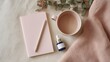 © CYBERPINK - Flat lay of a pink notebook, a pink mug, and a small blue dropper bottle on a white surface. the notebook is open and has a gold-colored pen resting on top of it.