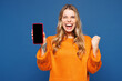 © ViDi Studio - Young happy excited woman wear yellow sweater casual clothes hold in hand use mobile cell phone with blank screen workspace area isolated on plain blue background studio portrait. Lifestyle concept.