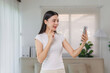 © amnaj - Young Asian woman smiling and talking during a video call on her mobile phone, communicating remotely from her living room