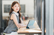 © PRIME STOCK LAB - Smiling young Asian woman sitting at a cafe counter using a digital tablet and looking at the camera.