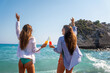 © NDABCREATIVITY - Two happy women toasting colorful beach drinks under the sun, enjoying tropical vibes and friendship