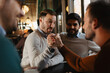 © Novak - Two men arm wrestling on a wooden table in a pub while their two friends watch closely and cheer them on during a fun night out.