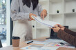 © Nittaya - Document Exchange in the Workplace: In a modern office setting, one person's hand reaches to receive documents from another, symbolizing efficient communication and collaborative efforts.