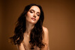 © Beauty Hero - Charming young woman with flawless makeup and wavy brunette hair posing against a beige background