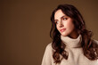 © Beauty Hero - Tender young woman with dark wavy hair wearing a beige turtleneck sweater against a solid background