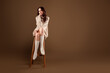 © Beauty Hero - Woman in cozy sweater seated on a chair, showcasing comfortable style and elegance against a beige studio background.