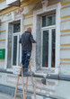 © Aleksandr - Worker on Ladder Renovating Building Facade with Bucket and Classical Architectural Details