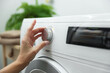© New Africa - Woman turning on white washing machine indoors, closeup