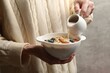 © New Africa - Woman pouring almond milk into bowl with oat flakes, nuts and blueberries on grey background, closeup