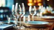 © vachom - A beautifully set dining table with wine glasses, plates, and cutlery under warm, cinematic lighting with soft bokeh in the background.