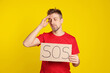 © New Africa - Unhappy man holding cardboard sign with word SOS on yellow background