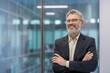 © Liubomir - Confident mature businessman with a beard and glasses smiling, crossing arms in a modern office, representing leadership, success, and professional expertise