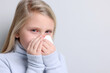 © New Africa - Little girl with tissue suffering from cold on grey background. Red eyes and nose
