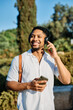 © Lumos sp - Young man enjoys sunny day while using smartphone and listening to music with earphones in urban setting, highlighting his joy and connection to the world around him